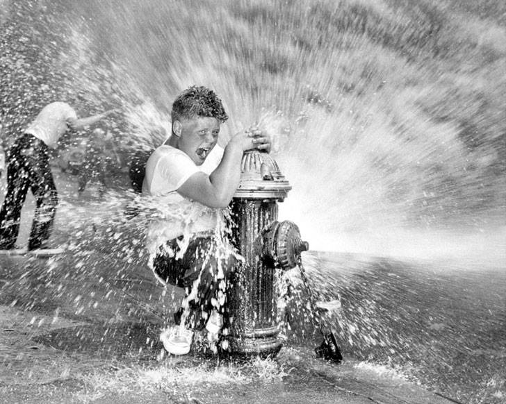 niño juega con el agua de un surtidor de los bomberos